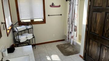 Ein Badezimmer mit Waschbecken, Handtuchhalter, Fenster, Duschvorhang und Holztür.