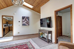 Amplia sala de estar con techo alto, televisor montado, mesa consola de madera con un florero y alfombra roja estampada.