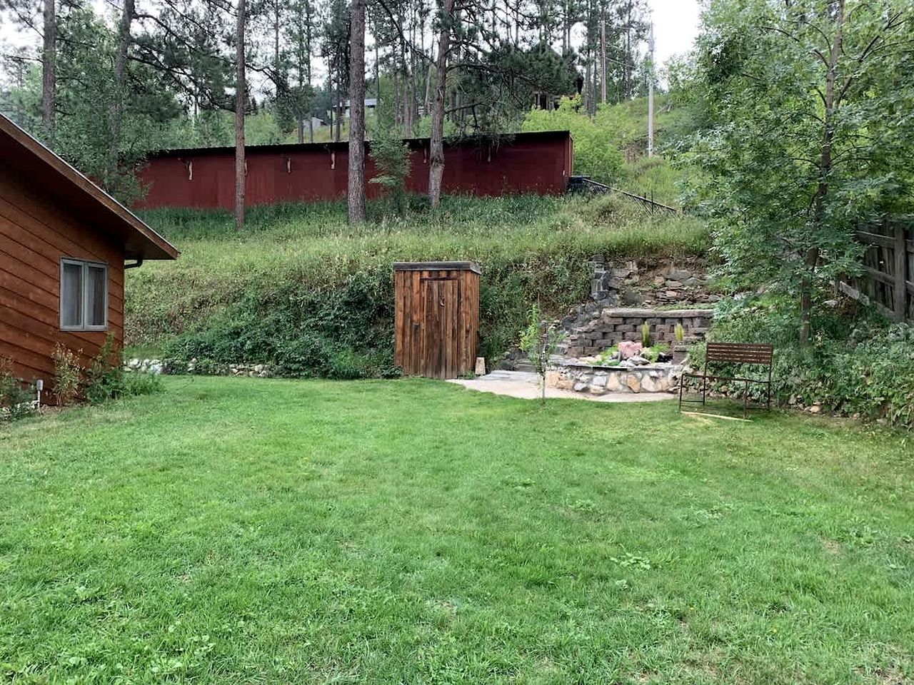 Una cabaña de madera con un cobertizo pequeño, una escalera de piedra y un patio cubierto de césped.