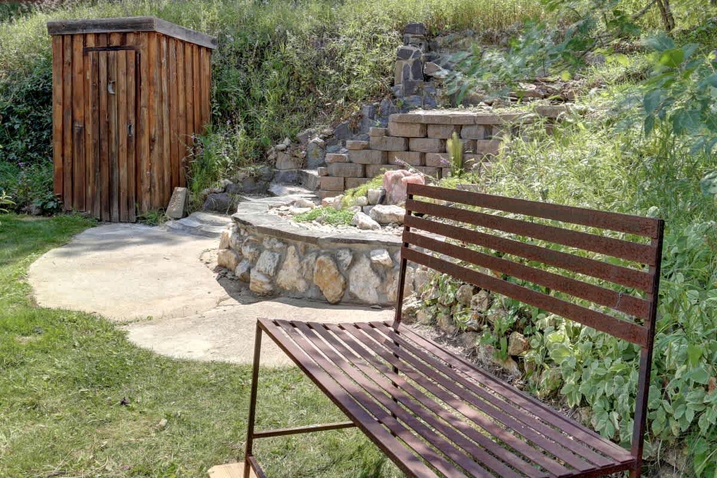 Eine hölzerne Bank und eine kleine Holzhütte in einem Garten mit einem gepflasterten Weg und Stufen.