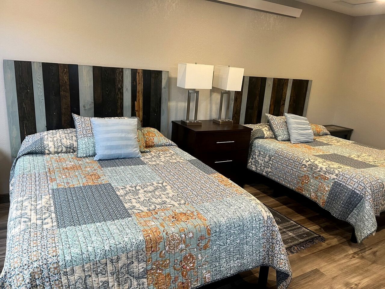 A hotel room with two beds, each with a patterned bedspread, a nightstand with a lamp, and a wooden headboard.