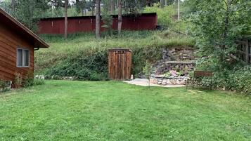 Eine Holzjagdhaushälfte mit einer kleinen Werkstatt, einer Steintreppe und einem Rasen.