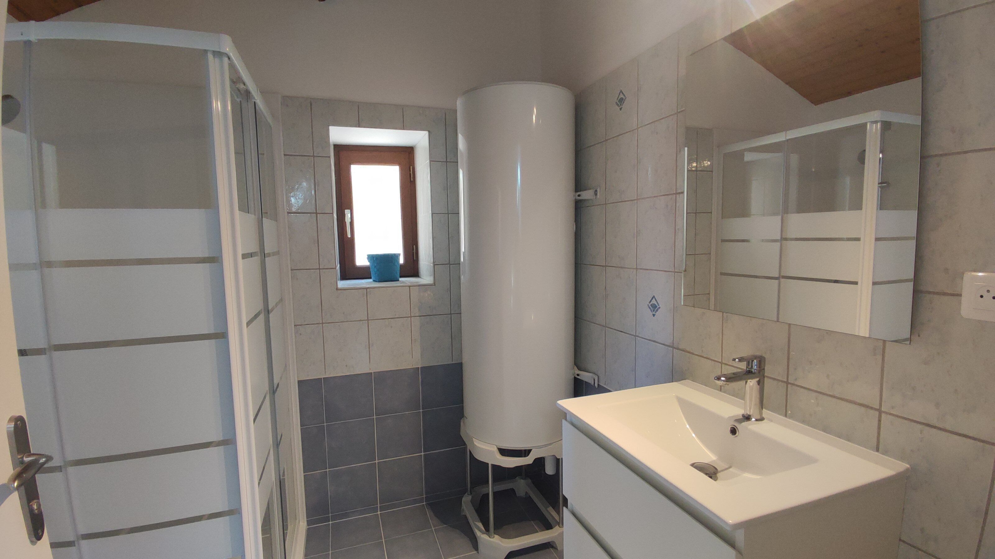 Une salle de bain avec une douche, un lavabo et une fenêtre.