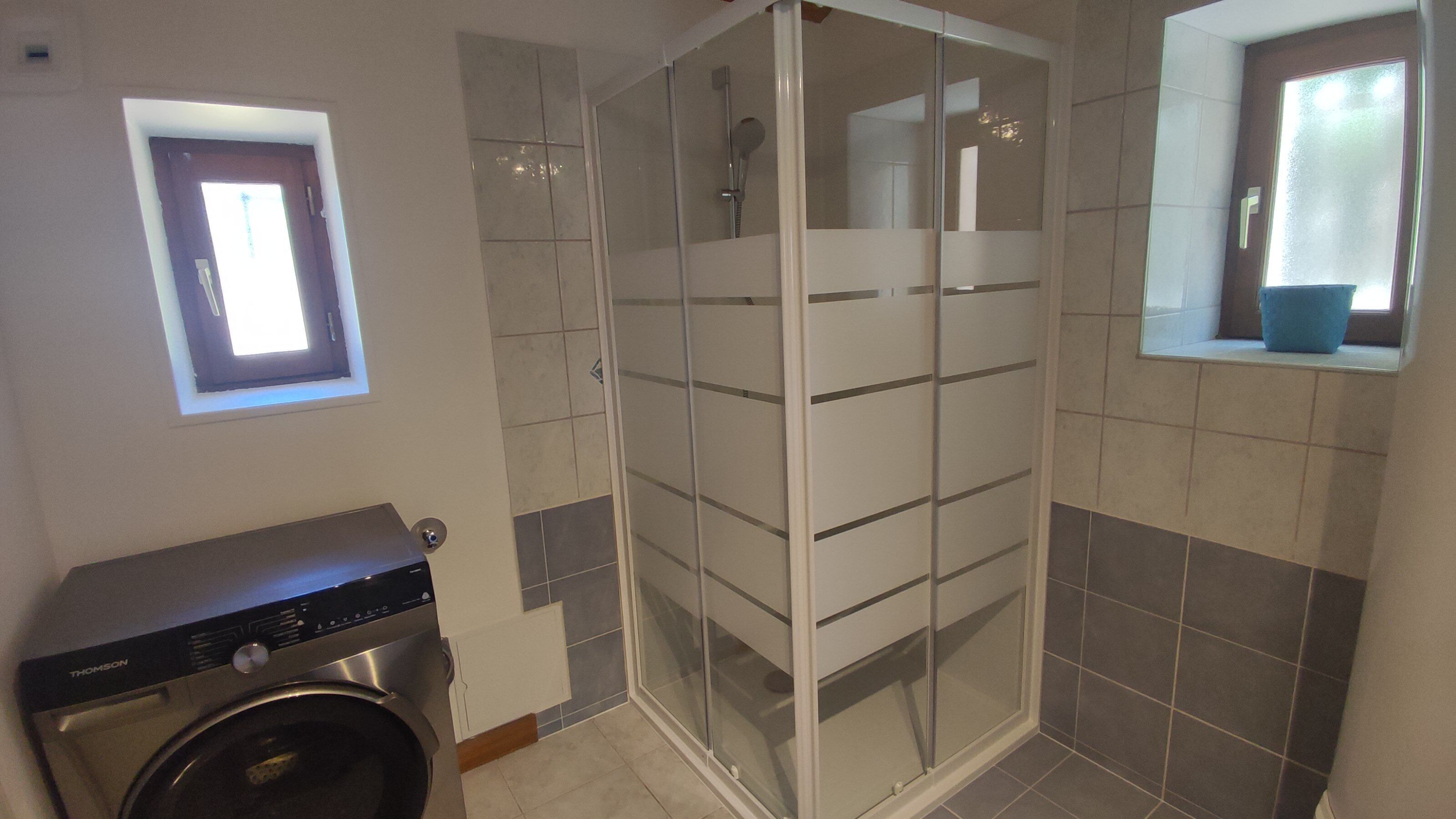 Ein Badezimmer mit Glasdusche, Waschmaschine und Fenster mit Aussicht.