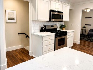 A kitchen with white cabinetry, a stainless steel microwave, an oven, and a marble countertop. - Cozy Getaway with Firepit, BBQ & Entertainment Room in Coeur d'Alene, Idaho (Coeur d'Alene)