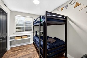 A bunk bed room with a window, a white console table, and a wall-mounted shelf. - Cozy Getaway with Firepit, BBQ & Entertainment Room in Coeur d'Alene, Idaho (Coeur d'Alene)