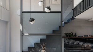 En modern inredning med ett runt matbord omgivet av stolar, en trappa och ett köksområde.