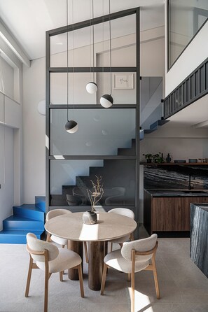 A modern interior with a round dining table surrounded by chairs, a staircase, and a kitchen area. - Cosmos Penthouse Suite (Chania)