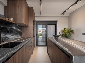 A modern kitchen with dark wood cabinets, a black marble countertop, and a black faucet. - Cosmos Penthouse Suite (Chania)