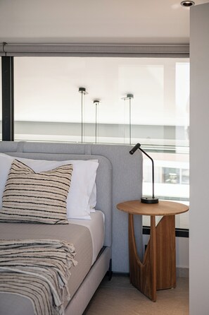 A modern bedroom with a bed, a bedside table, and a window with a view. - Cosmos Penthouse Suite (Chania)