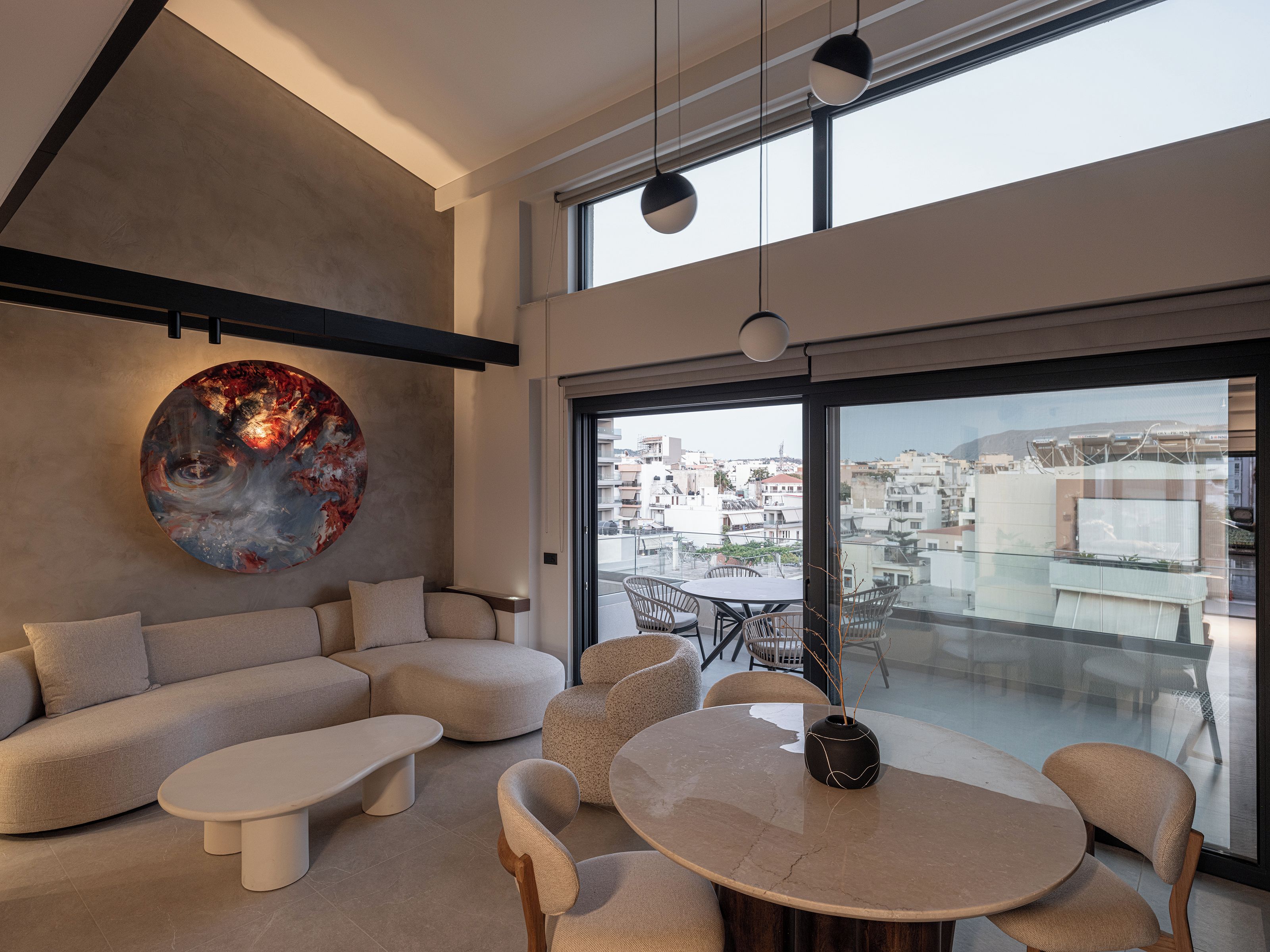 Un intérieur moderne avec un canapé, une table basse et une table à manger avec des chaises. Un grand tableau abstrait orne le mur, et de grandes fenêtres offrent une vue sur la ville.
