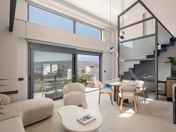 Ein modernes Wohnzimmer mit Glastür zum Balkon, ausgestattet mit Sofas, Sesseln und einem Couchtisch.