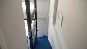 En trappa med blåa trappsteg som leder upp till en liten plattform med en dörr och en ljusströmbrytare på väggen.
