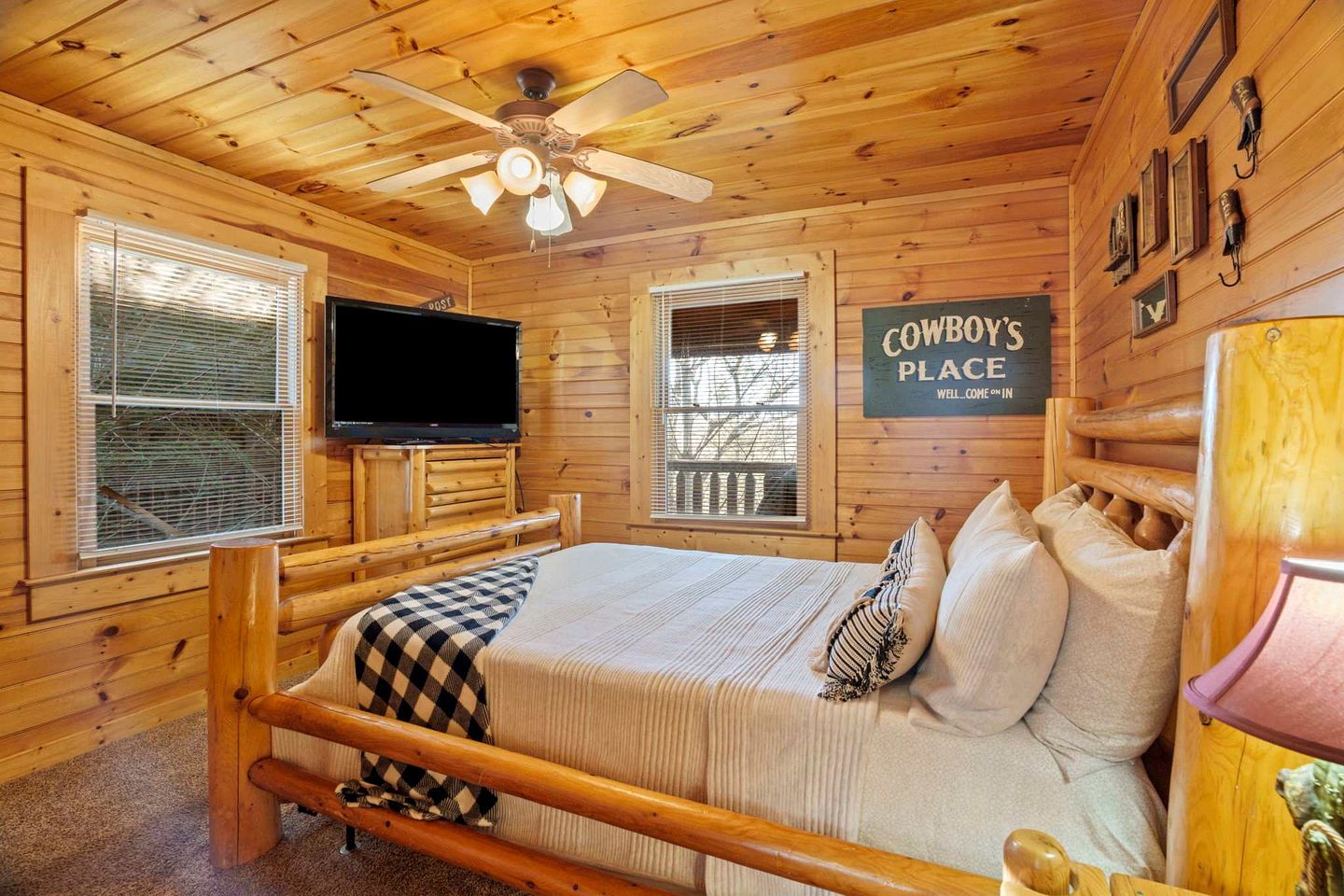 A wooden cabin room with a bed, a television, and a sign reading 'COWBOYS PLACE.'