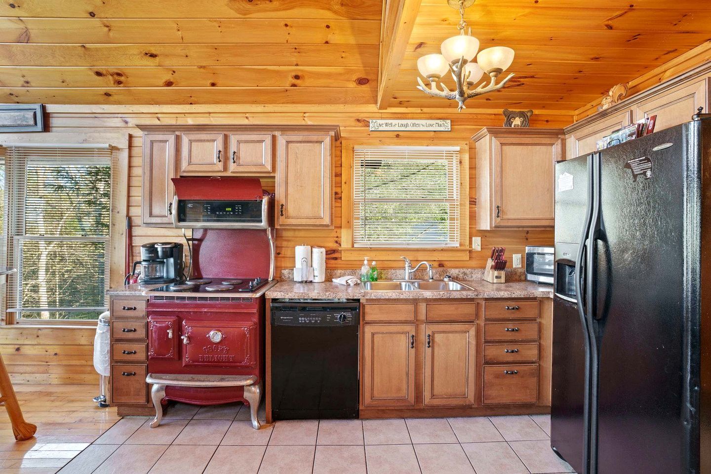 A kitchen with wooden cabinets, a red stove, a black dishwasher, and a black refrigerator.