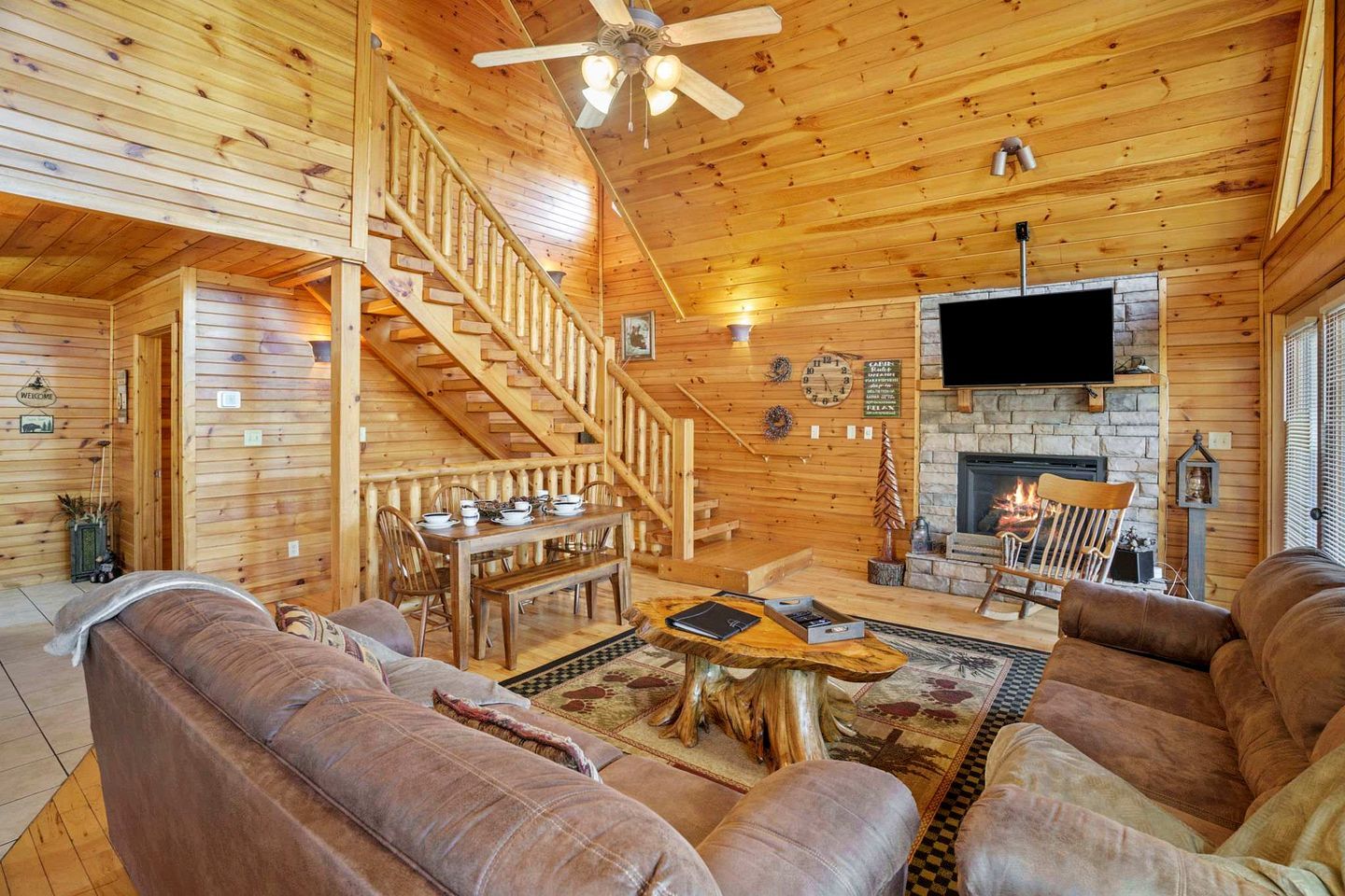 L’intérieur d’une cabane en rondins, avec un escalier en bois, une cheminée, un téléviseur à écran plat et un coin salon confortable.