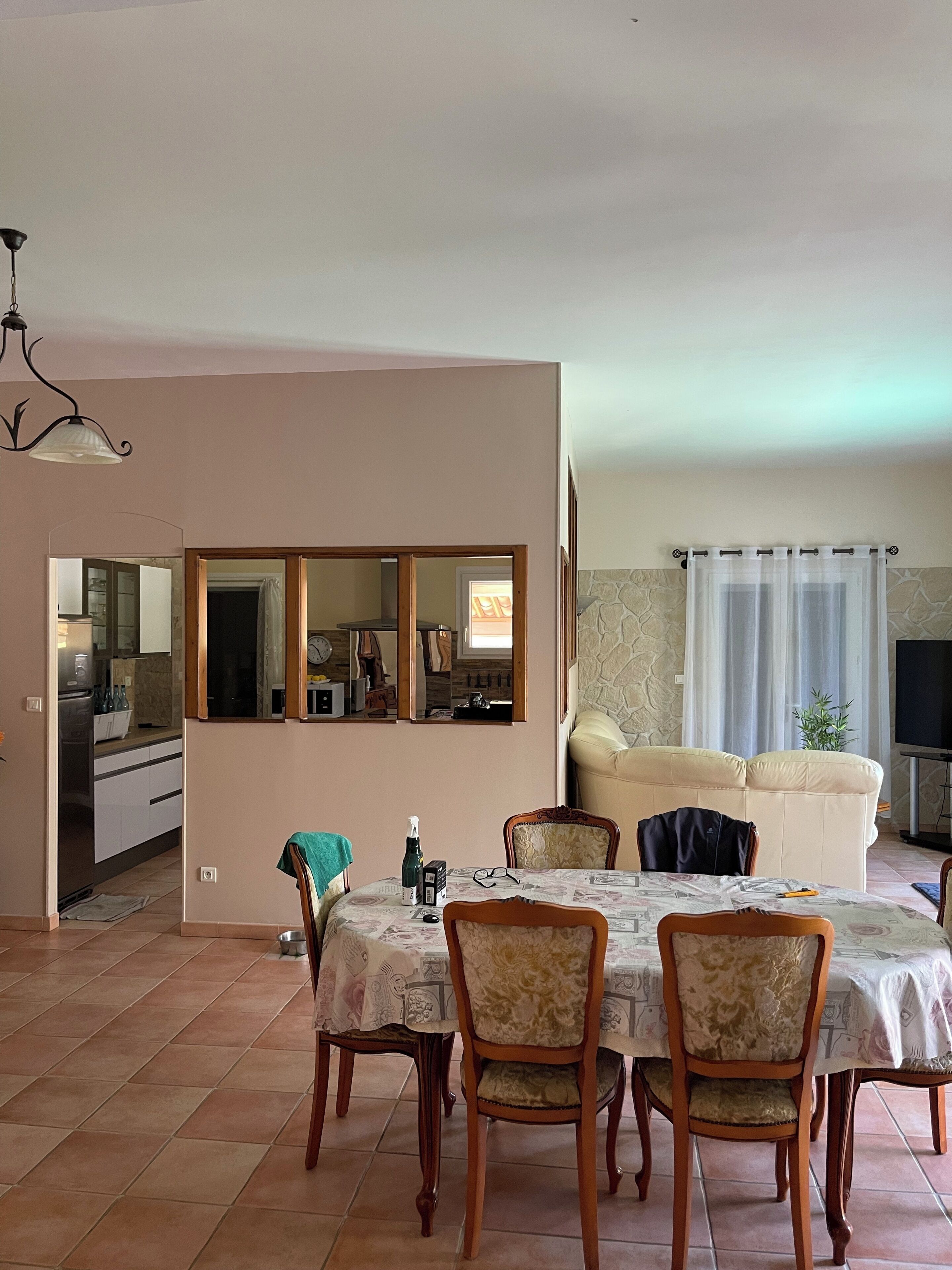 Una zona de menjador amb taula preparada per a quatre, sofà, televisió i cuina visible a través d'una porta oberta.