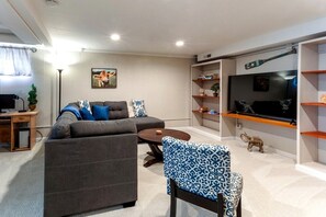 A modern living room with a sectional sofa, a coffee table, a TV, and a bookshelf. - Family-Friendly Home with Fire Pit & Cozy Fireplace in Coeur d'Alene, Idaho (Coeur d'Alene)