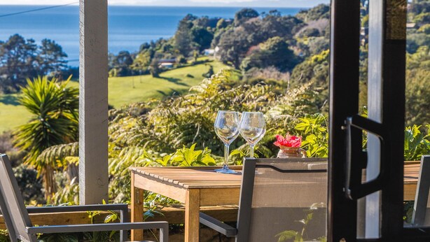 Ein Tisch mit zwei leeren Weingläsern und einer Vase mit einer Blume, mit Blick auf eine malerische Landschaft mit Meer- und Hügellandschaft.