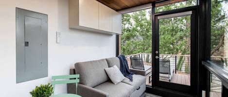 A modern room with a grey sofa, a small table with a plant, and a balcony with outdoor furniture.