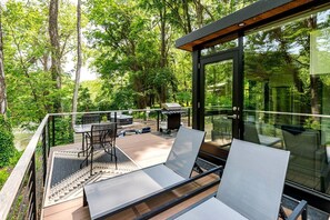 Una terraza moderna al aire libre con paredes de vidrio, mobiliario de metal y zona de parrillada.