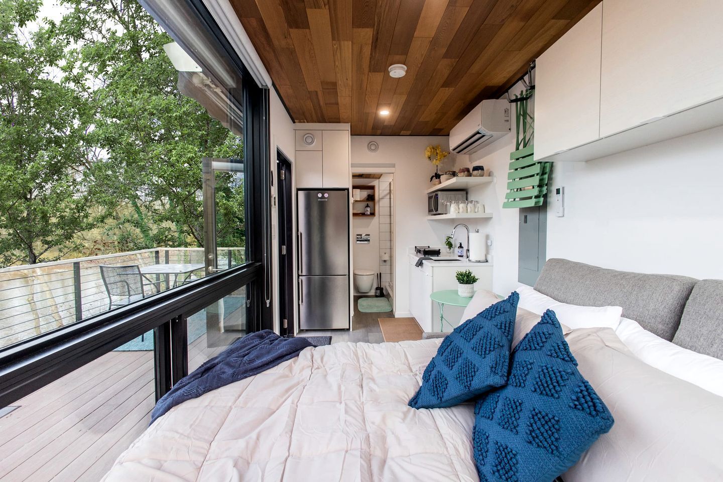 A modern bedroom with a large bed, a view of the outdoors, a kitchenette, and a dining area.