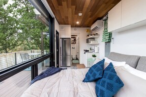 Quarto moderno com cama grande, vista para o exterior, cozinha compacta e área de jantar.