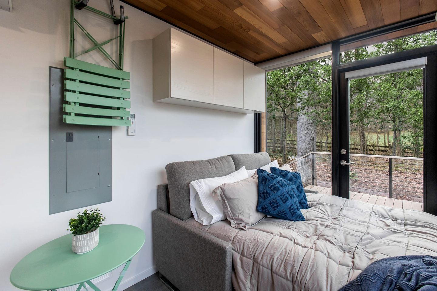 A bedroom with a bed, a small table, a potted plant, and a view of the outdoors.