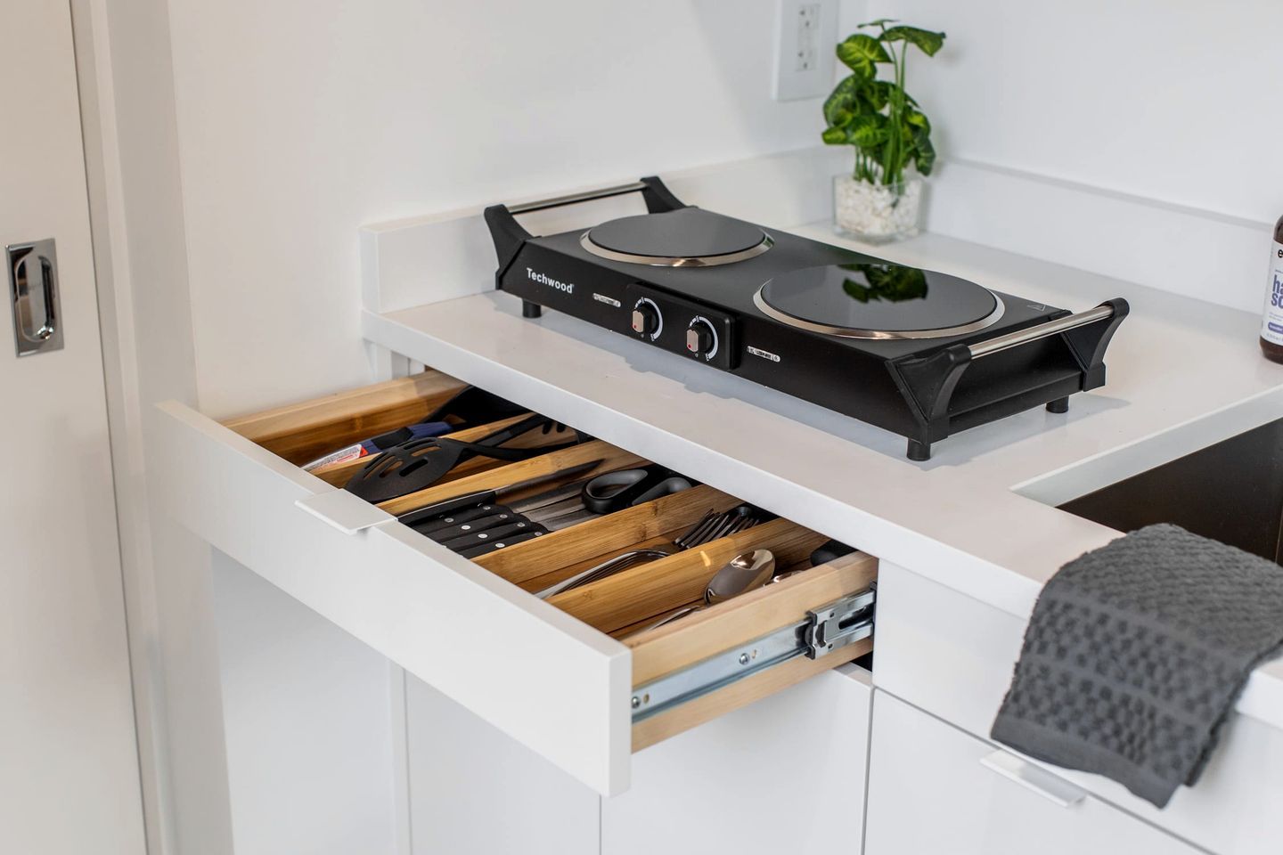 A kitchen with a black stove, a drawer with utensils, and a small plant on the counter.