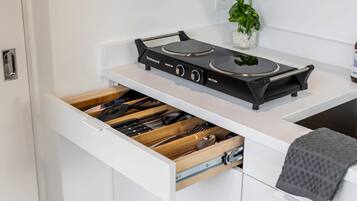 A kitchen with a black stove, a drawer with utensils, and a small plant on the counter.
