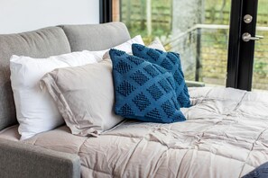 Una cama con edredón color beige, dos almohadas y una manta tejida azul.