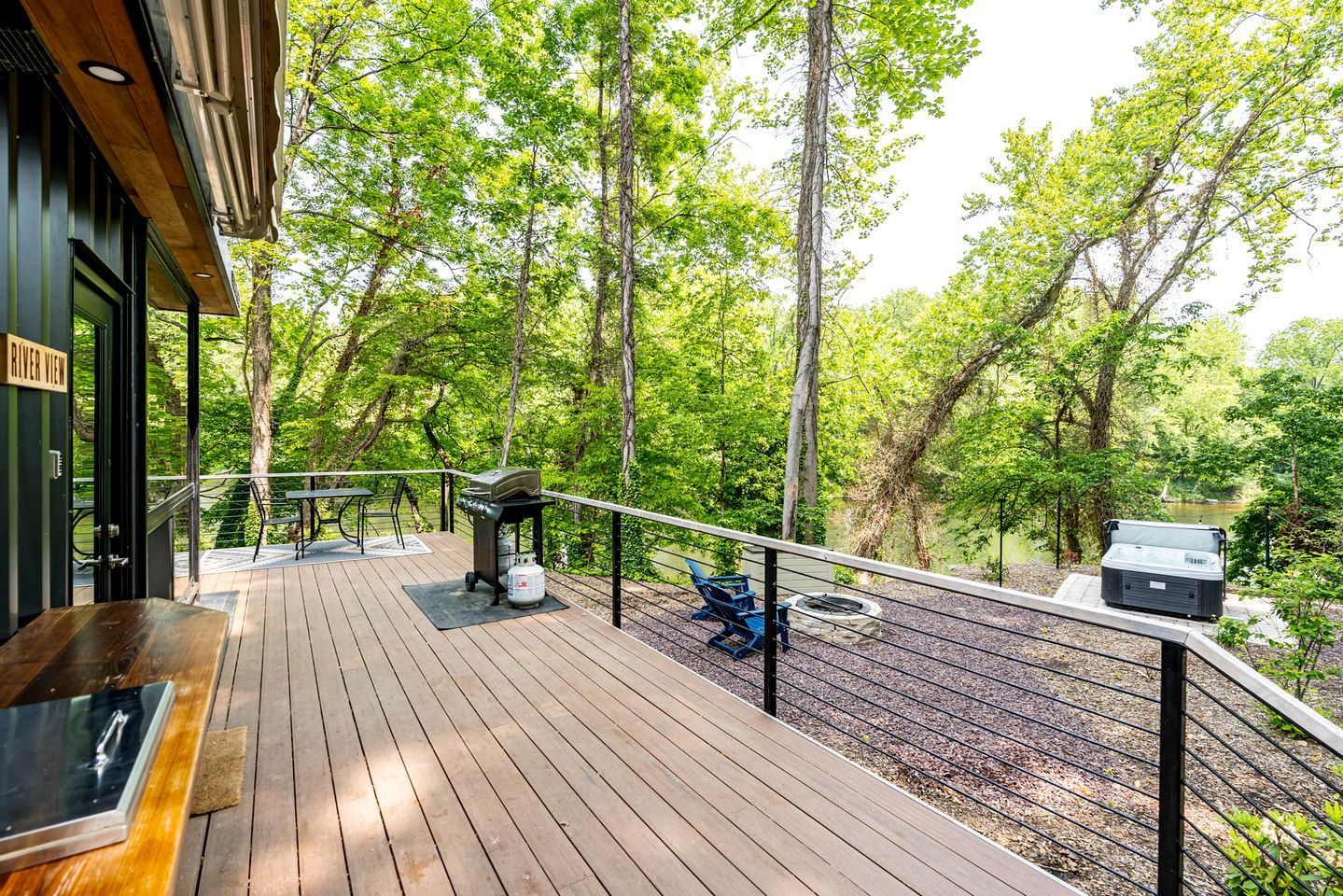 A wooden deck with a grill, chairs, and a table, overlooking a forested area.