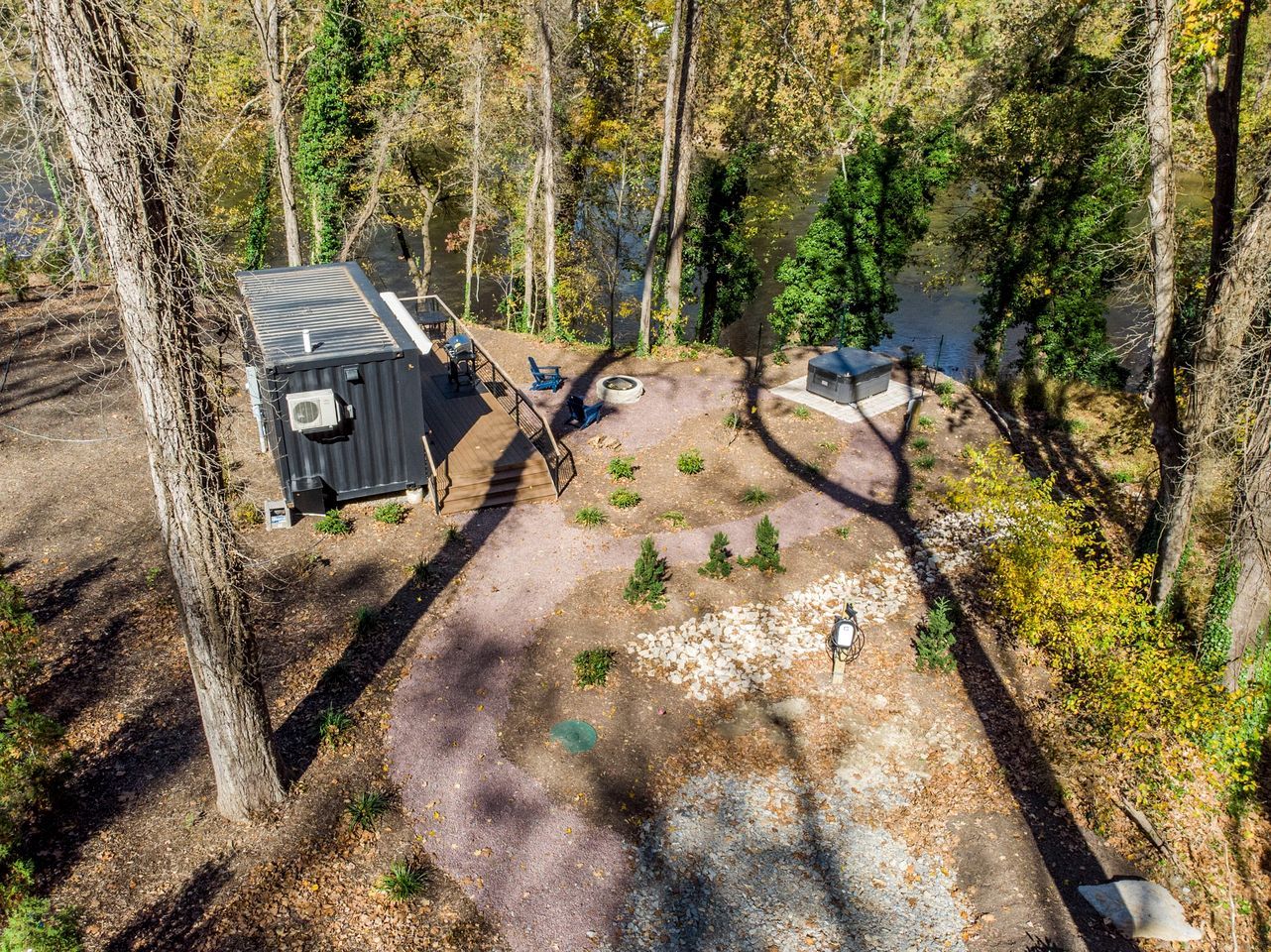 A cabin with a small deck, a fire pit, and a pond in a forested area.