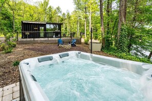Uma banheira de hidromassagem em meio à floresta, com uma cabana ao fundo.
