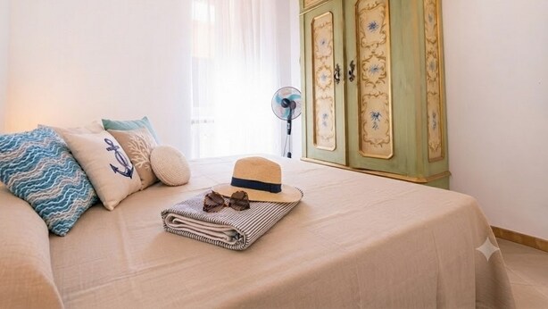 A bedroom with a bed, pillows, a hat, sunglasses, and a fan. - Appartamento il Corsaro (Imperia)