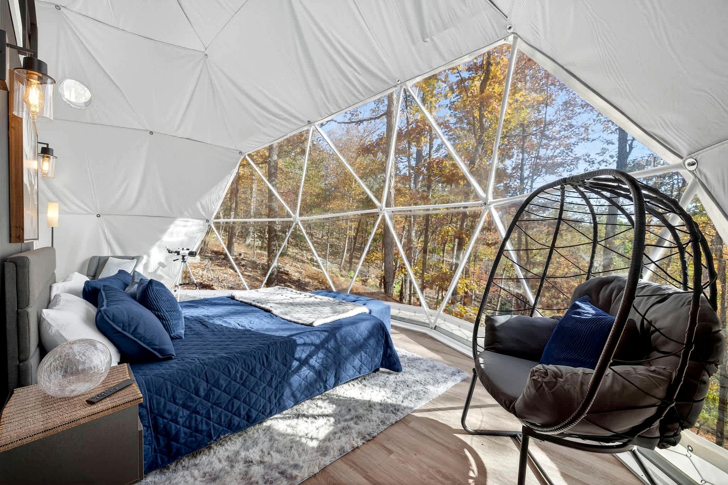 A tent with a bed, a hanging chair, and a view of trees.
