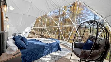 Una carpa con cama, una silla colgante y vista a los árboles.