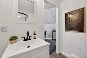 Un bagno con un lavandino bianco, uno specchio, una pianta in vaso e un quadro appeso al muro.