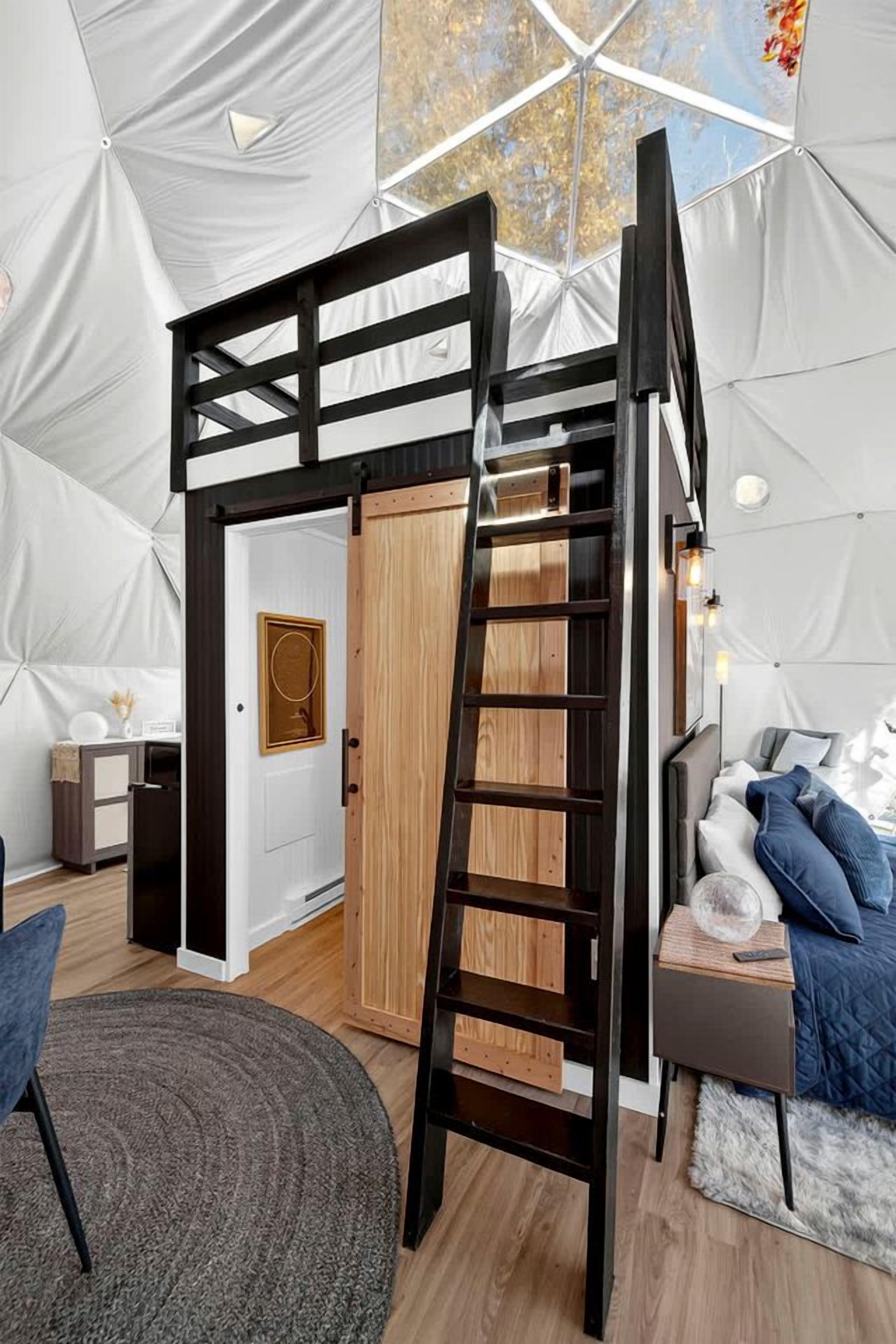 A tented room with a bunk bed, a ladder, a desk, and a chair.