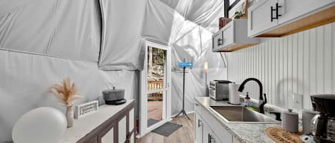 A compact kitchen with a sink, stove, and cabinets, under a large tent-like structure.