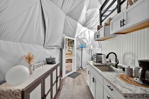 Una cocina pequeña con pileta, estufa y alacenas, bajo una gran estructura tipo tienda de campaña.