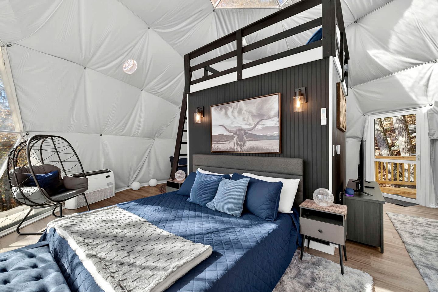 Een tentvormige kamer met een bed, een hangstoel, een bureau en een wandlamp.