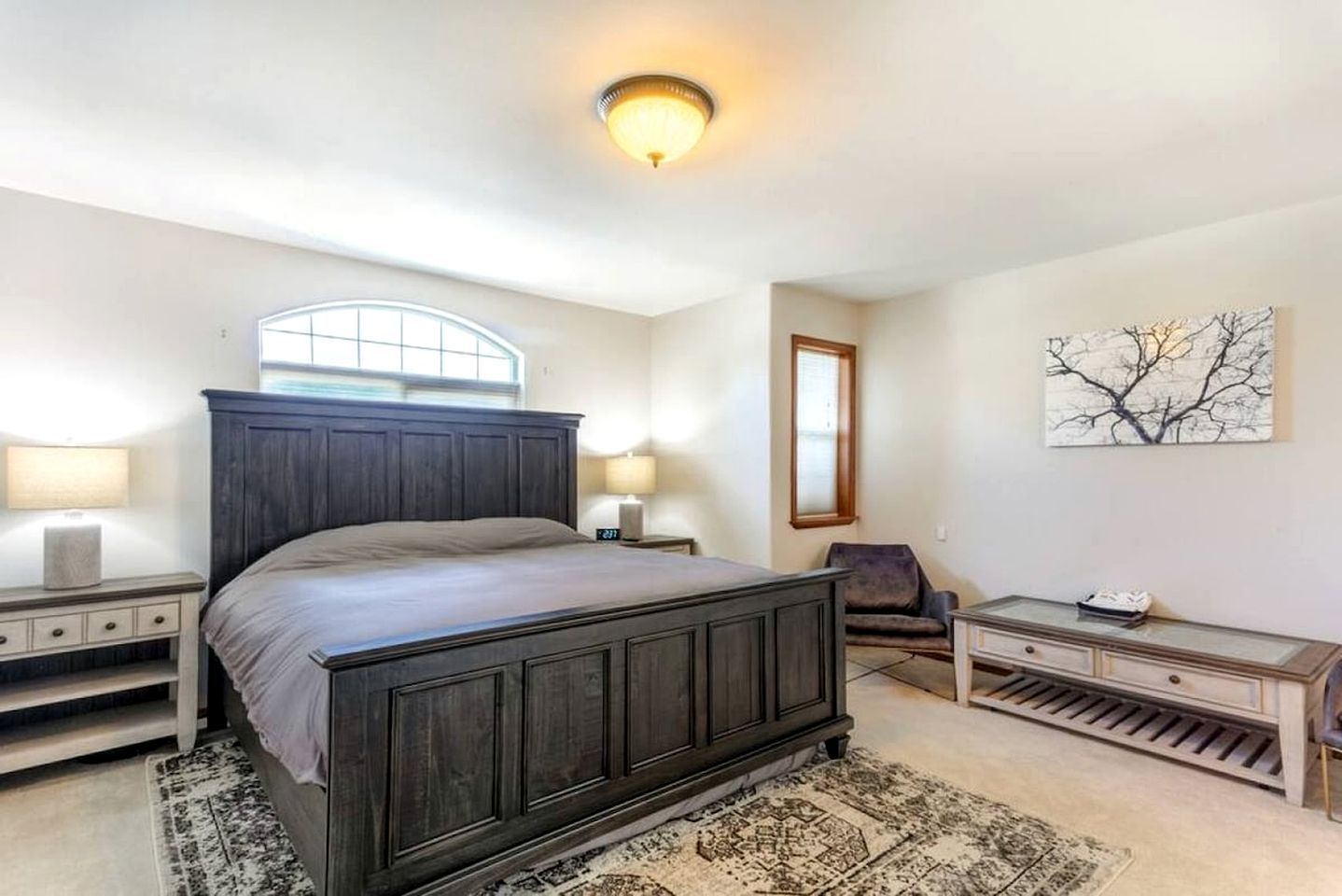 A bedroom with a large bed, bedside tables, a chair, a desk, and a window.