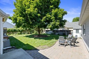 Un jardin avec une terrasse, un arbre et une clôture.