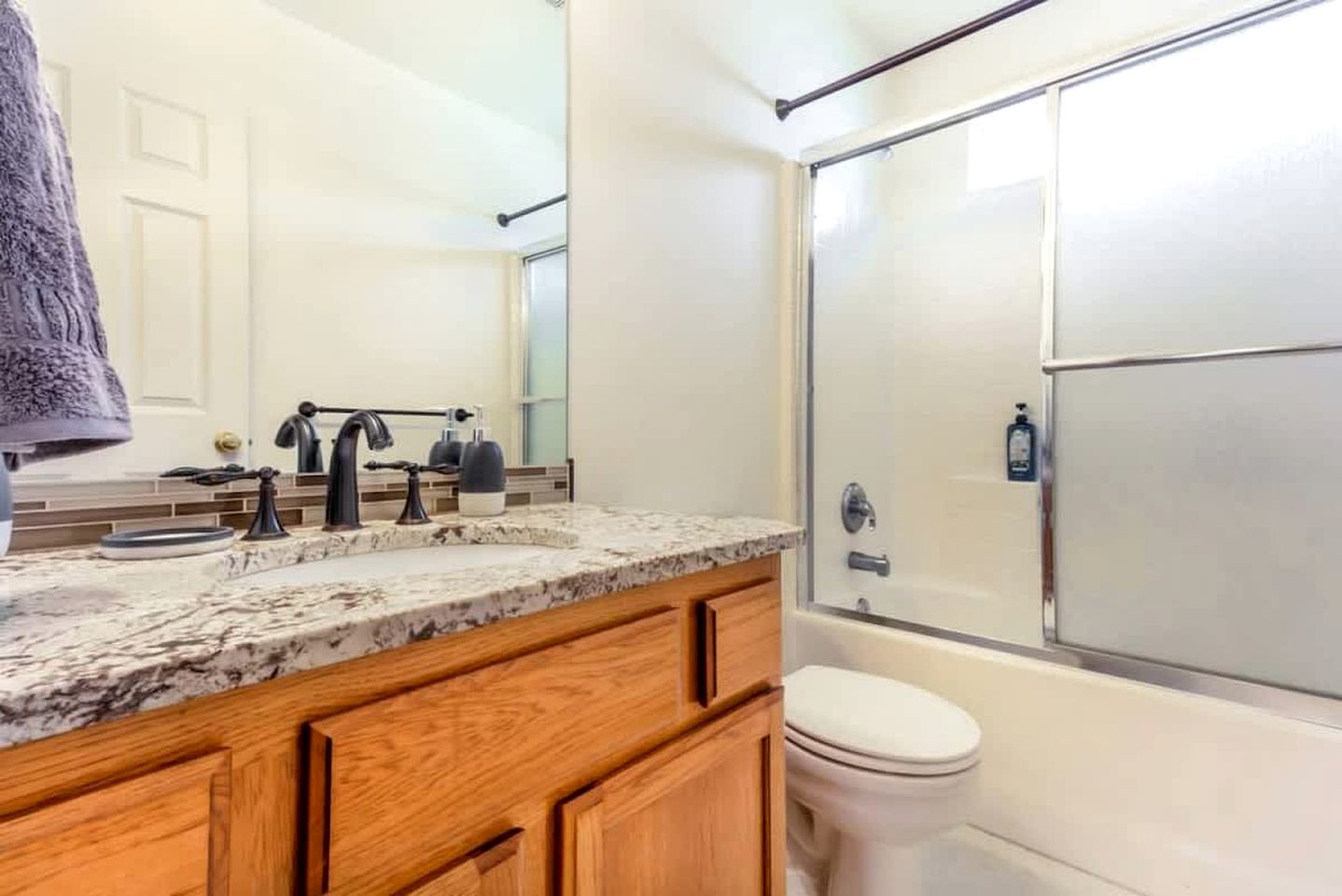 A bathroom with a marble countertop, wooden cabinets, a white toilet, and a glass-enclosed shower.