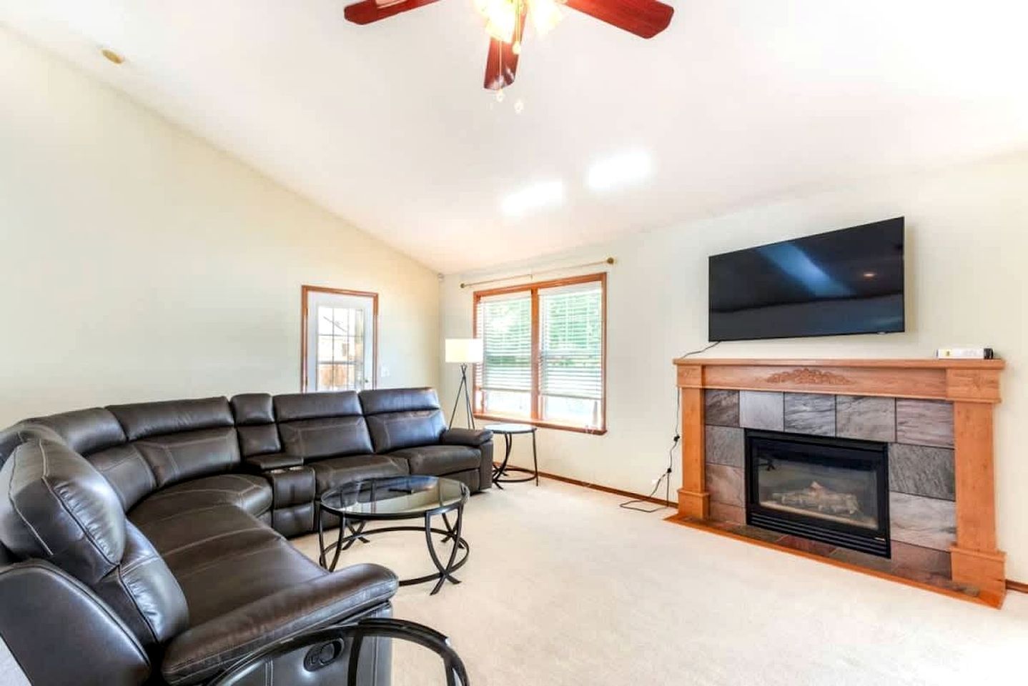 A living room with a sectional sofa, a fireplace, a flat-screen TV, and a ceiling fan.