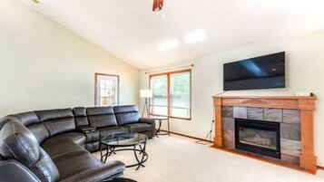 A living room with a sectional sofa, a fireplace, a flat-screen TV, and a ceiling fan.