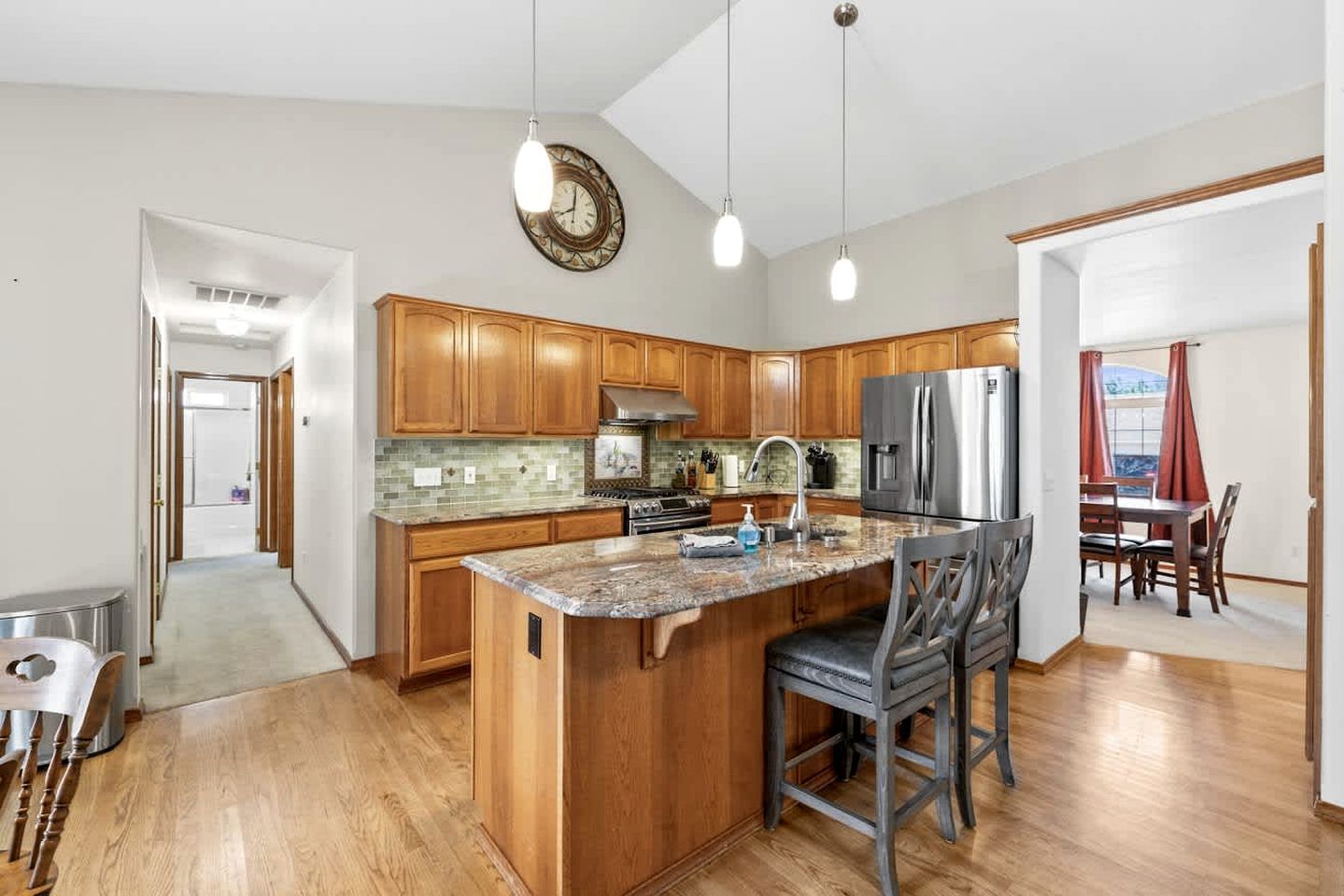 A modern kitchen with wooden cabinets, a central island, stainless steel appliances, and pendant lighting.