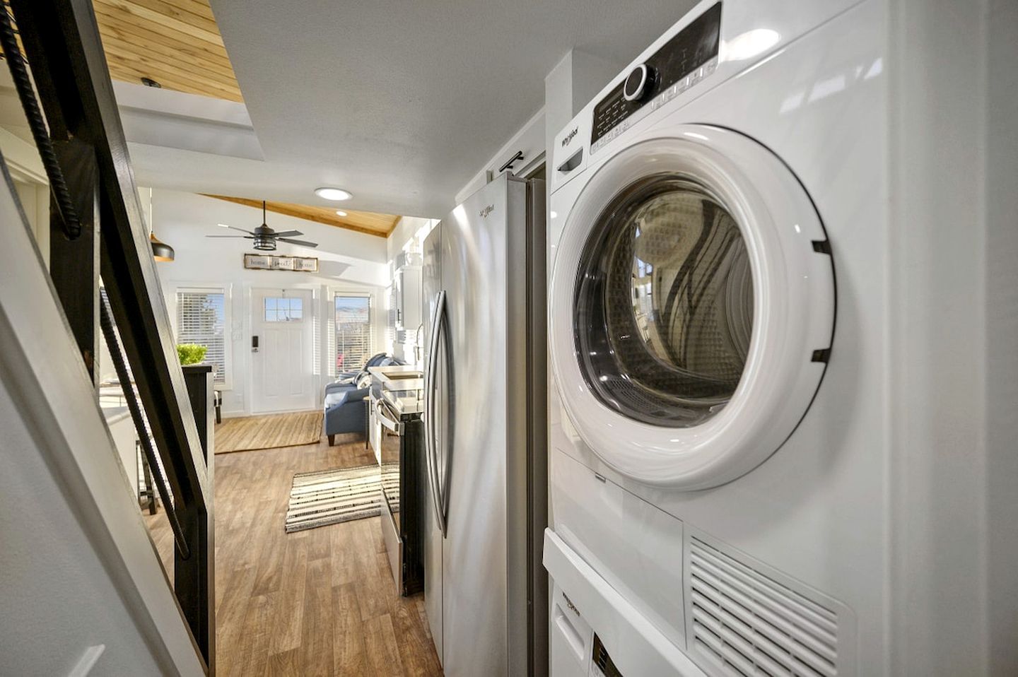 A laundry room with a front-loading washer and dryer, wooden flooring, and a ceiling fan.