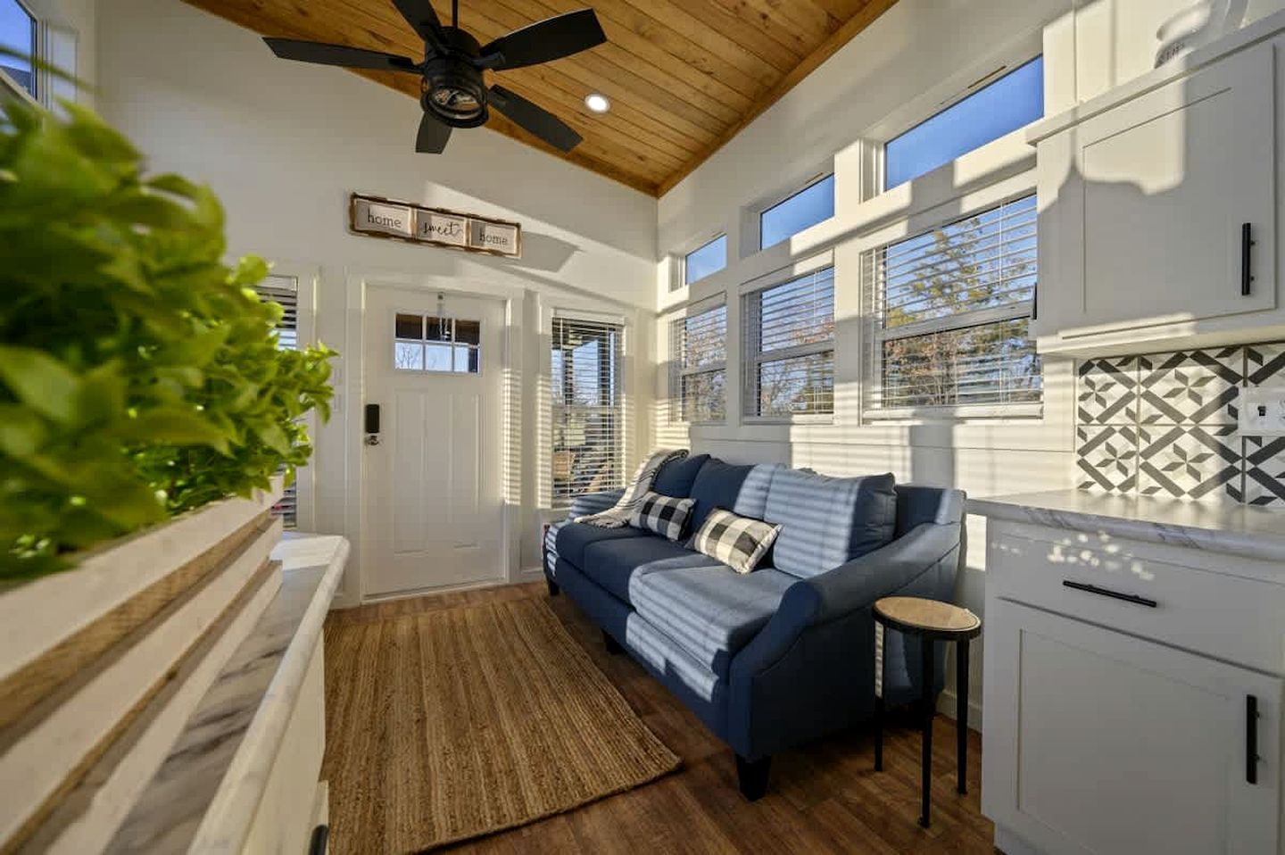 A modern kitchen with white cabinets, a blue sofa, and a ceiling fan.